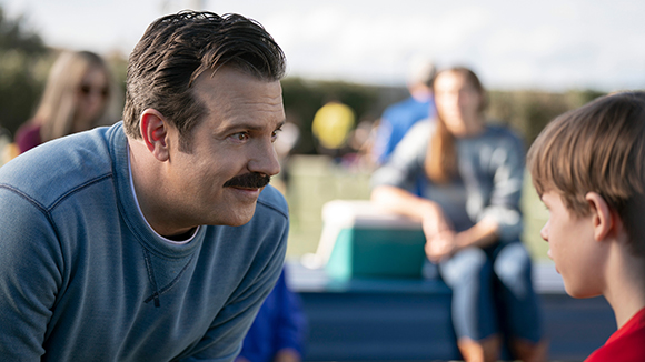 A man with a mustache leans in to look closely at a young boy outdoors.