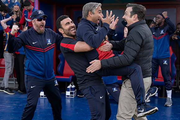 Men in blue and red athletic gear cheering and embracing during a sporting event.