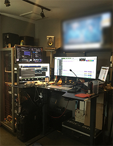 A desk with multiple computer monitors, studio monitors, and audio equipment in a dimly lit room.