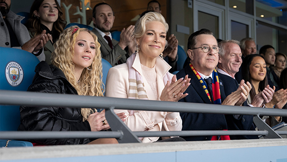 A group of people in a stadium seating area clapping and smiling.