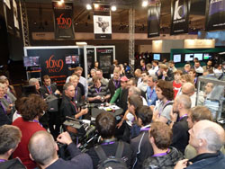 A large group of people crowd around a display booth at a professional convention.