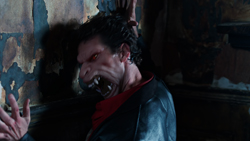 A pale man with sharp teeth and dark hair looks upward in a dimly lit room.