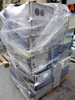 A large stack of various computer towers wrapped tightly in clear plastic stretch film on a wooden pallet.