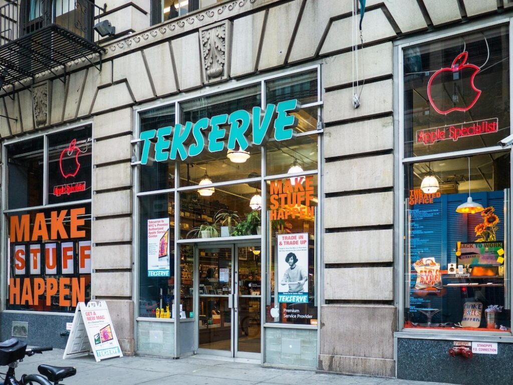 The glass storefront of Tekserve with a large blue sign and Apple logos in the windows.