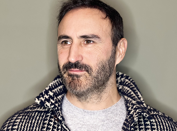 A man with dark hair and a salt-and-pepper beard looking to the side.