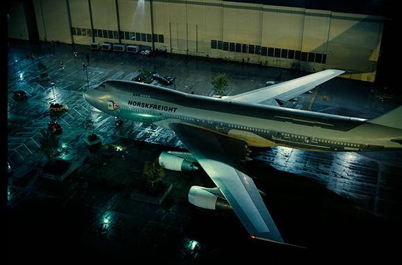 A large Norsk Freight cargo plane parked on a wet airport tarmac at night under bright lights.