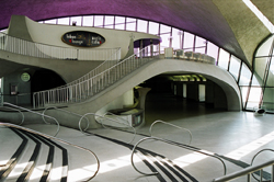 Curved concrete staircase and balcony inside a building with large arched windows and a purple ceiling.