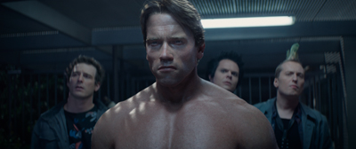 A muscular man looks intensely forward with three men standing in the background.