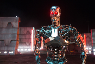A silver metallic robot with glowing red eyes stands against a dark, industrial background with red lights.