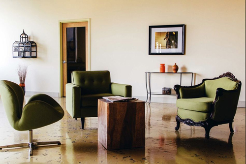 Green armchairs, a wooden block table, and a slim console table in a room with polished concrete floors.
