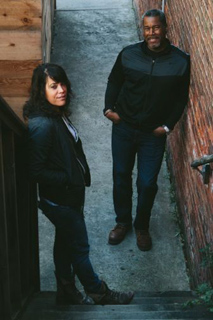 A man in a black jacket and a woman in a dark jacket stand in a narrow alleyway.