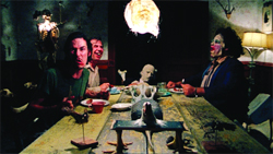People sitting at a long table in a dark room under a bright hanging light.