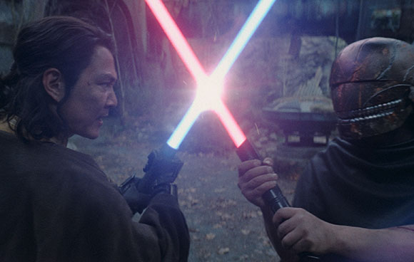 Two people in profile facing off with red and blue glowing energy swords.