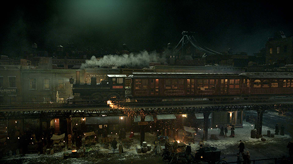 A steam train moves across an elevated track above a dimly lit, snowy city street at night.