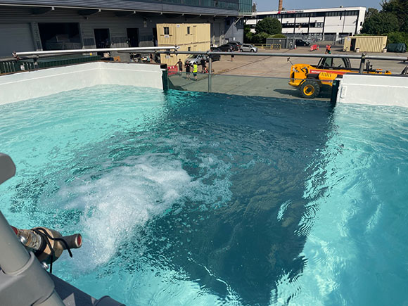 A large rectangular pool filled with turquoise water showing ripples and white bubbles.