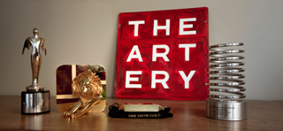 Various gold and silver trophies and a red sign reading THE ARTERY on a wooden table.