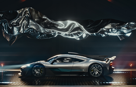 A silver supercar parked on a dark, slatted floor under a large, floating piece of wavy silver fabric.