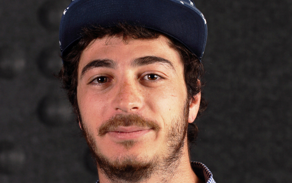 A man with dark curly hair and a beard wearing a dark blue baseball cap.