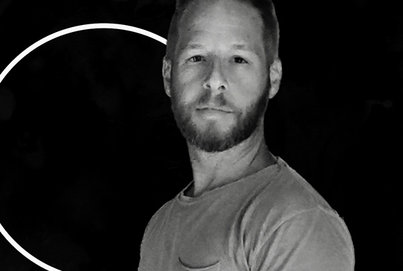 Black and white portrait of a man with a short beard and a light-colored t-shirt.