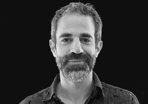 Black and white headshot of a man with curly hair and a full beard looking forward.