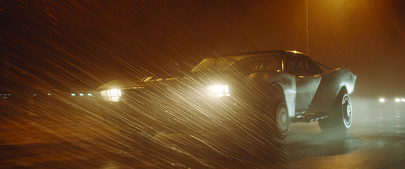 A dark car driving through heavy rain illuminated by bright headlights at night.