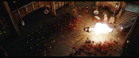High-angle shot of a grand, dark hall with overturned chairs and a bright white explosion on the floor.