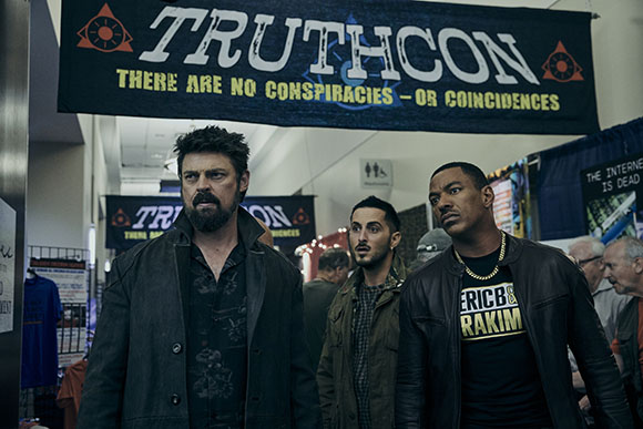 Three men stand in a convention hall beneath a large black banner that reads TRUTHCON.