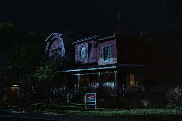 A dark, red, Victorian-style house at night with a sold sign in the front yard.