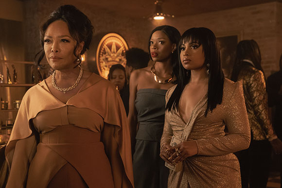 Three women in elegant evening dresses stand together in a warm, dimly lit indoor setting.