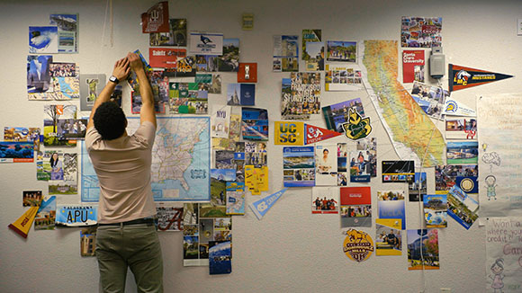 A person stands before a wall densely covered in various university posters, maps, and flyers.
