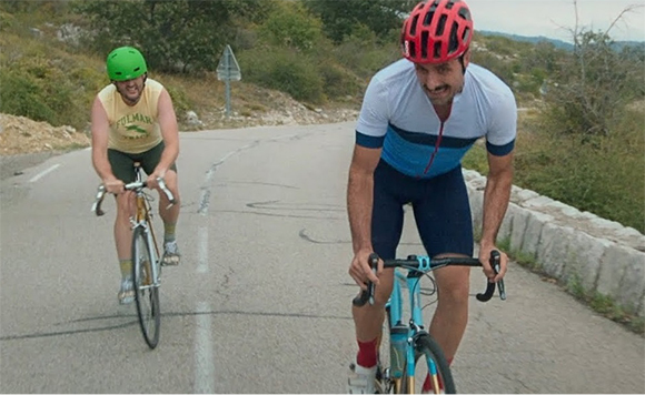 Two men cycling on a paved mountain road through a green landscape.