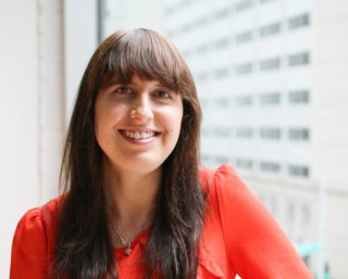 A smiling woman with long brown hair and bangs wearing a bright red blouse.