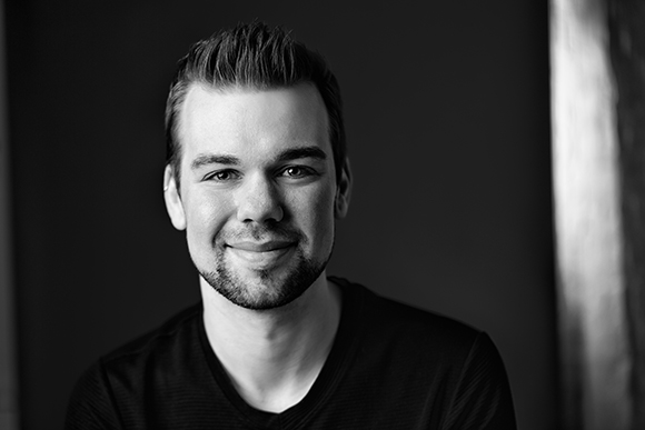 A smiling man with short spiked hair and a light beard looking toward the camera.