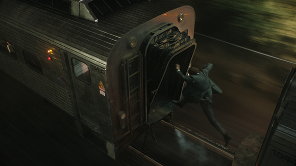 A person in a dark suit leaps between two moving subway train cars at night.
