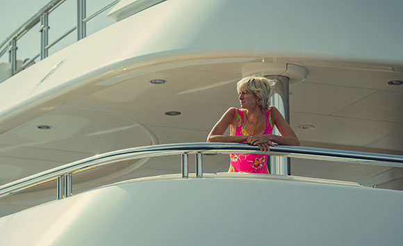 A woman in a pink swimsuit leans on the silver railing of a large white yacht.