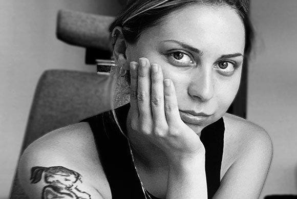 Black and white close-up of a woman looking at the camera with her hand resting on her cheek.