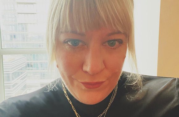 Close-up portrait of a woman with blonde hair and bangs looking toward the camera.