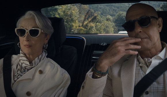 An older woman in white sunglasses and a man in dark sunglasses sitting in the back of a vehicle.
