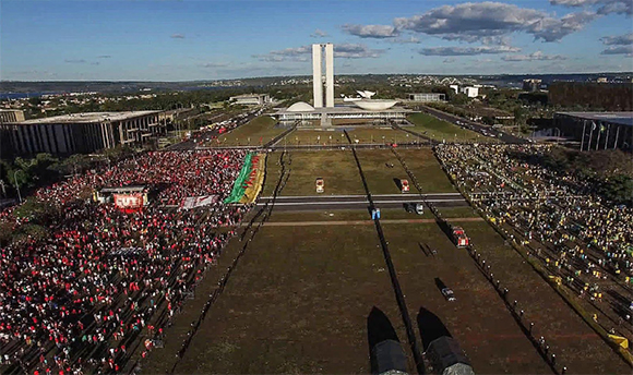 Aerial view of large crowds gathered on a wide plaza in front of the National Congress in Brasilia.