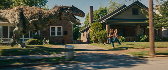 A large bipedal dinosaur walks past suburban houses while two people run across a lawn.
