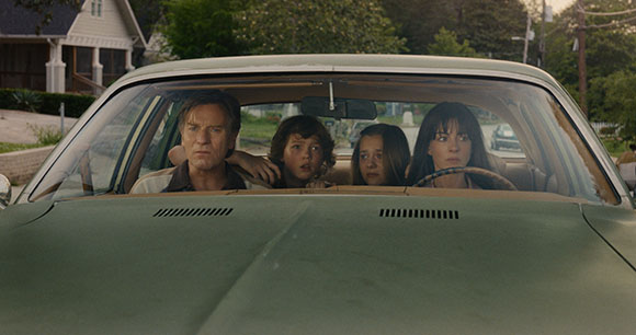 A man, two children, and a woman sit inside a green car, looking ahead with serious expressions.
