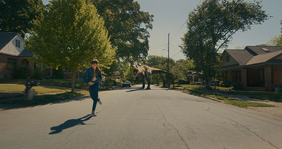 A person runs down a sunny residential street as a large dinosaur stands in the distance.
