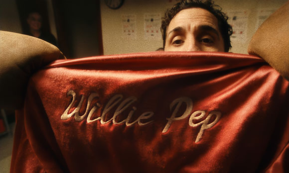 A man looks over a red velvet fabric with the name Willie Pep embroidered in gold script.