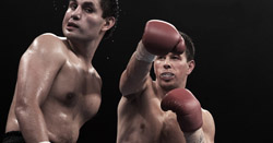 A boxer in red gloves throws a punch toward his opponent against a dark background.