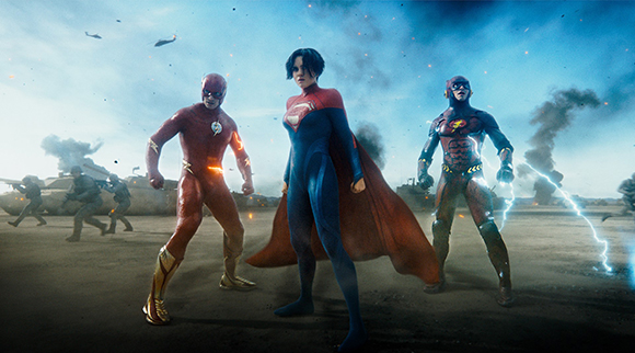 Three superheroes in colorful suits stand amidst a smoky battlefield with soldiers and tanks in the background.