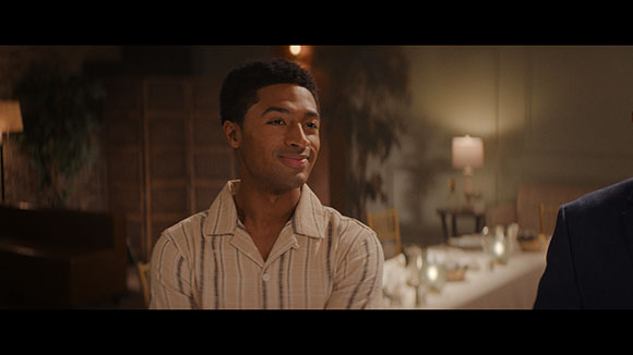A man in a striped shirt smiles while sitting in a dimly lit restaurant.