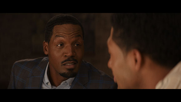 A man in a blue plaid blazer looks intently at a person in profile.