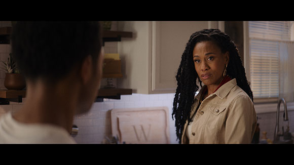 A woman with long dark braids looks toward a man in a kitchen setting.
