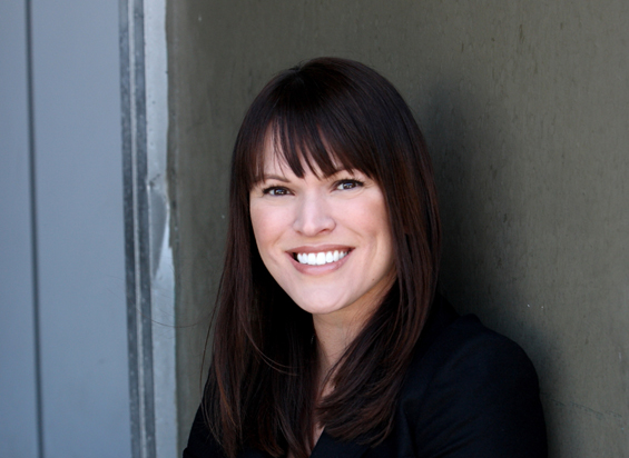 A smiling woman with long dark hair and bangs wearing a black top.