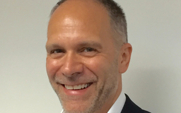 A smiling man with light skin, short hair, and a graying beard looking toward the camera.